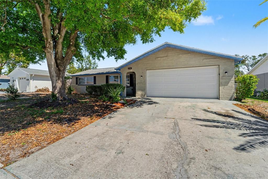 A single-story house with a beige brick facade, a two-car garage, and a large tree — 7744 WATERFORD STREET, NEW PORT RICHEY, FL