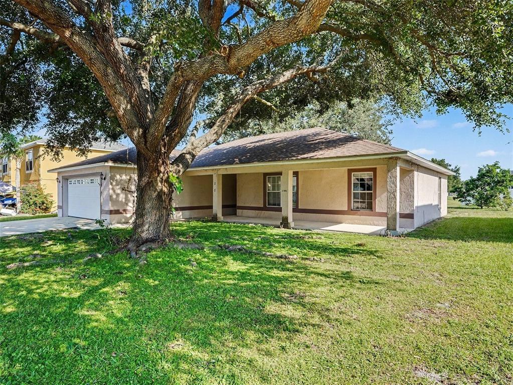 A single-story house with a tan stucco exterior, a covered porch, and a large oak tree — 121 SHADDOCK DRIVE, AUBURNDALE, FL