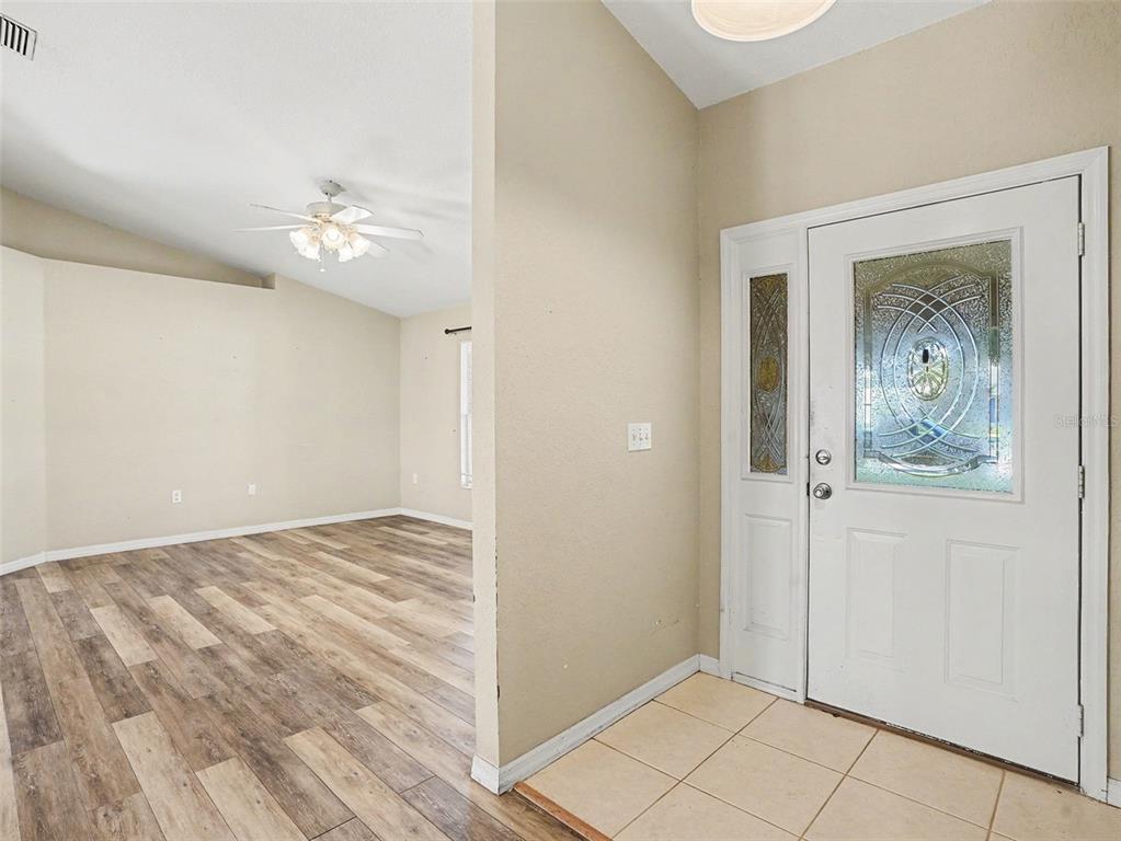 An entryway with a tiled floor leads into a living room with wood-look flooring — 121 SHADDOCK DRIVE, AUBURNDALE, FL