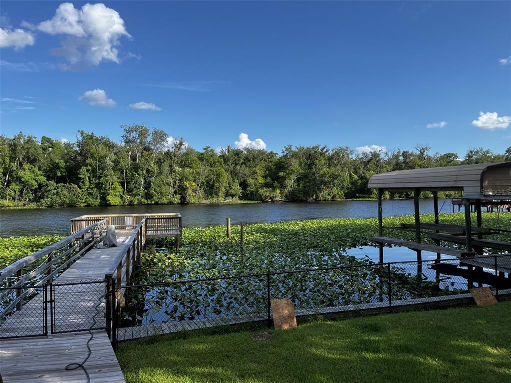 A wooden dock and a boat lift extend into a lake covered in lily pads — 334 PARADISE CIRCLE, SATSUMA, FL