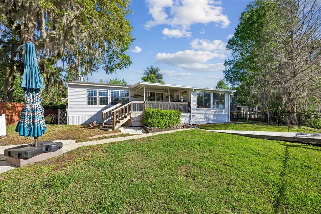 A single-story mobile home with a wooden deck and stairs sits on a grassy lot — 334 PARADISE CIRCLE, SATSUMA, FL