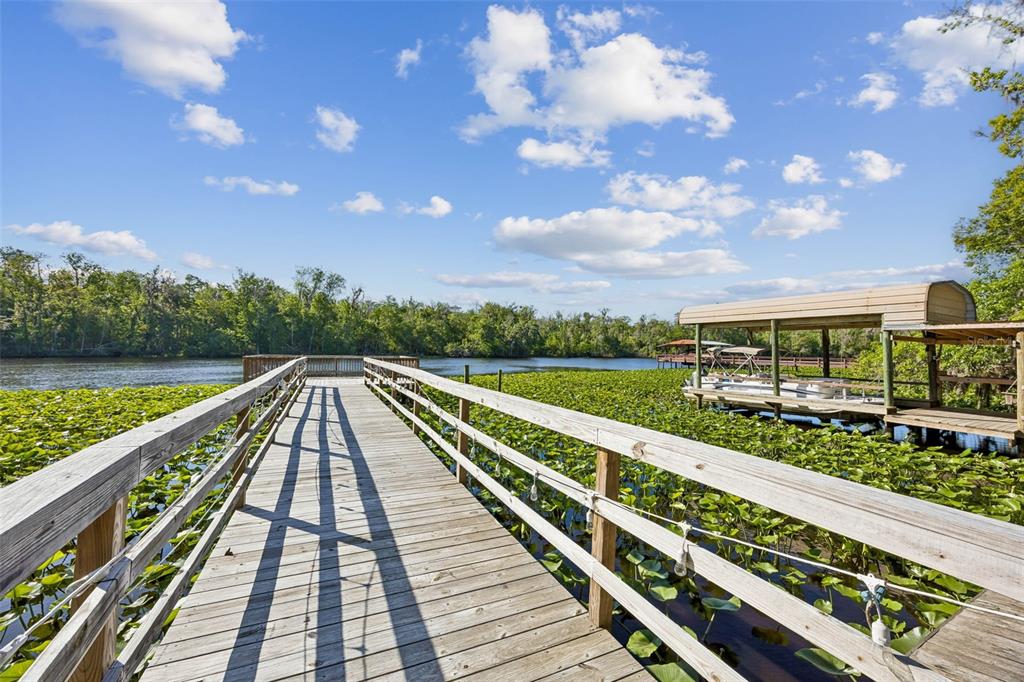 A wooden dock extends over a water lily-covered lake toward a covered boat slip — 334 PARADISE CIRCLE, SATSUMA, FL
