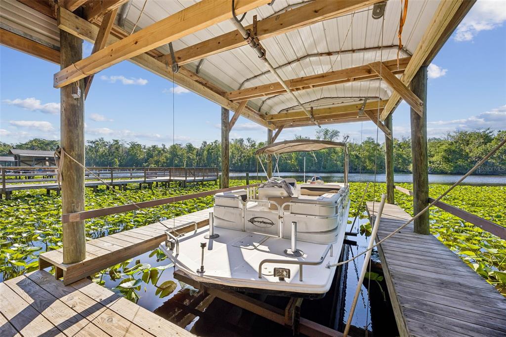 A pontoon boat is docked under a covered wooden boat lift on a lake — 334 PARADISE CIRCLE, SATSUMA, FL