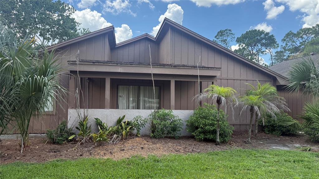 A brown house with vertical siding and a covered porch sits behind a landscaped yard — 250 RAINTREE DRIVE, CASSELBERRY, FL