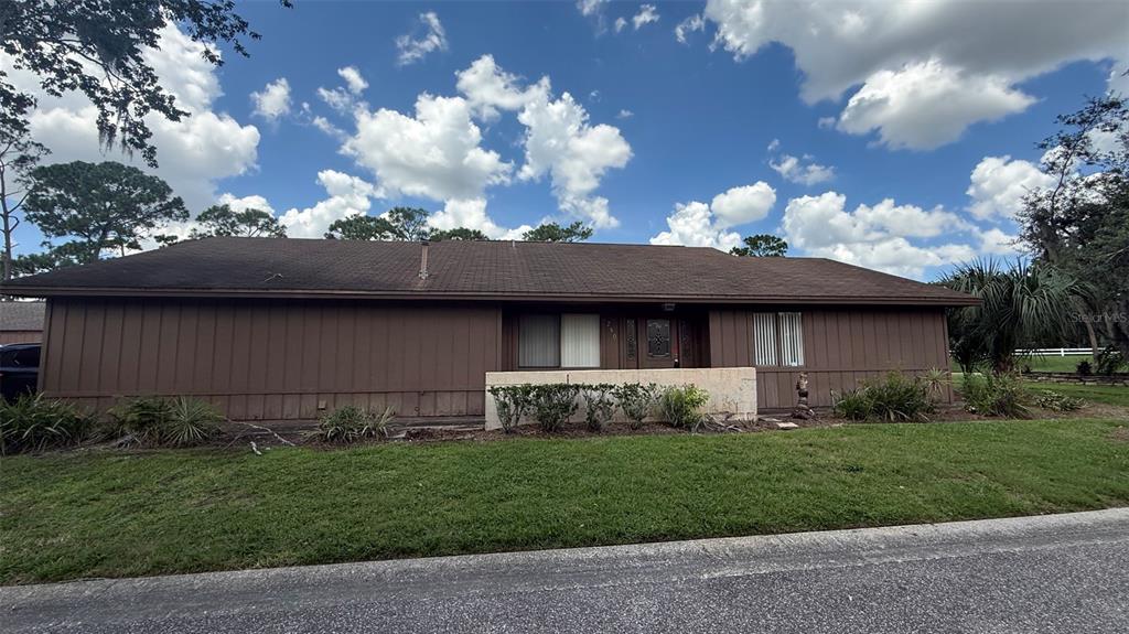 A single-story house with brown vertical siding and a low-sloped roof under a cloudy sky — 250 RAINTREE DRIVE, CASSELBERRY, FL