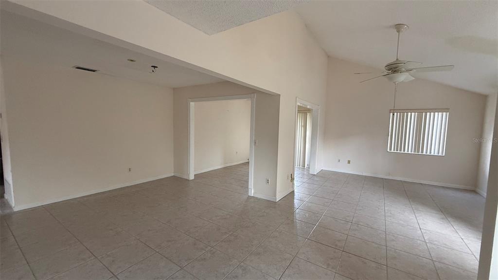 An open living area features light-colored tile flooring, vaulted ceilings, and a ceiling fan — 250 RAINTREE DRIVE, CASSELBERRY, FL