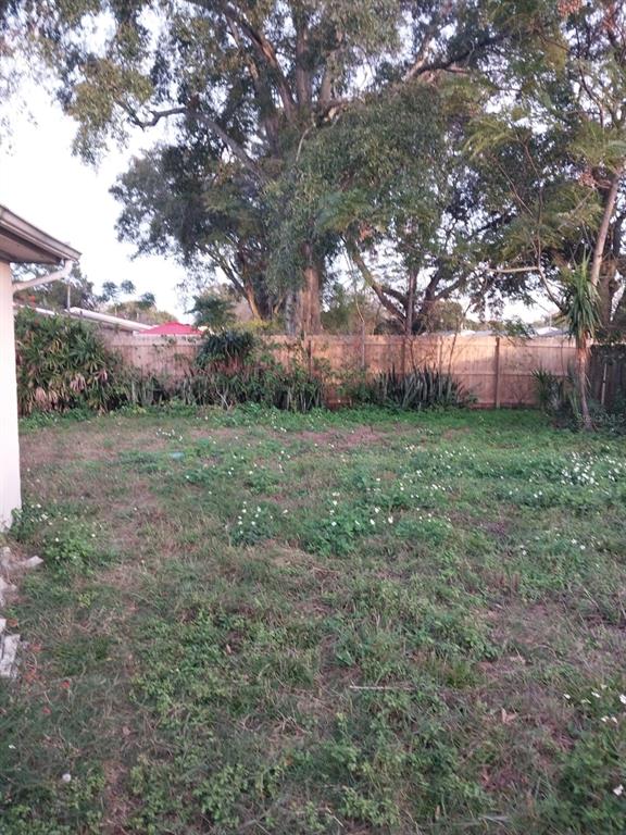 A grassy backyard features a wooden fence, mature trees, and various shrubs — 5032 VALIMOR DRIVE, HOLIDAY, FL