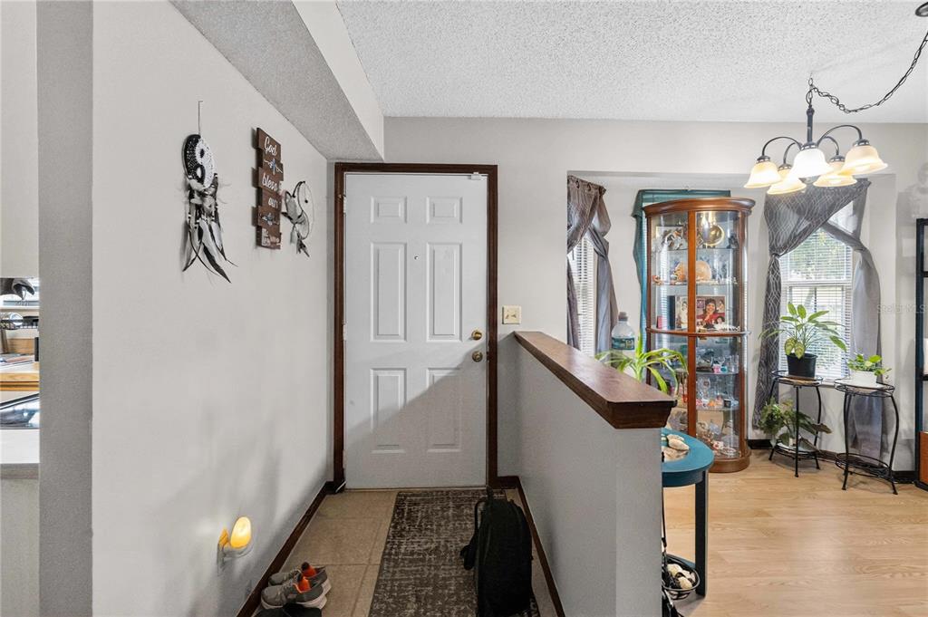 An entryway features a white front door, tile flooring, and a half-wall overlooking a dining area — 4807 COACHMANS DRIVE UNIT 2402, ORLANDO, FL