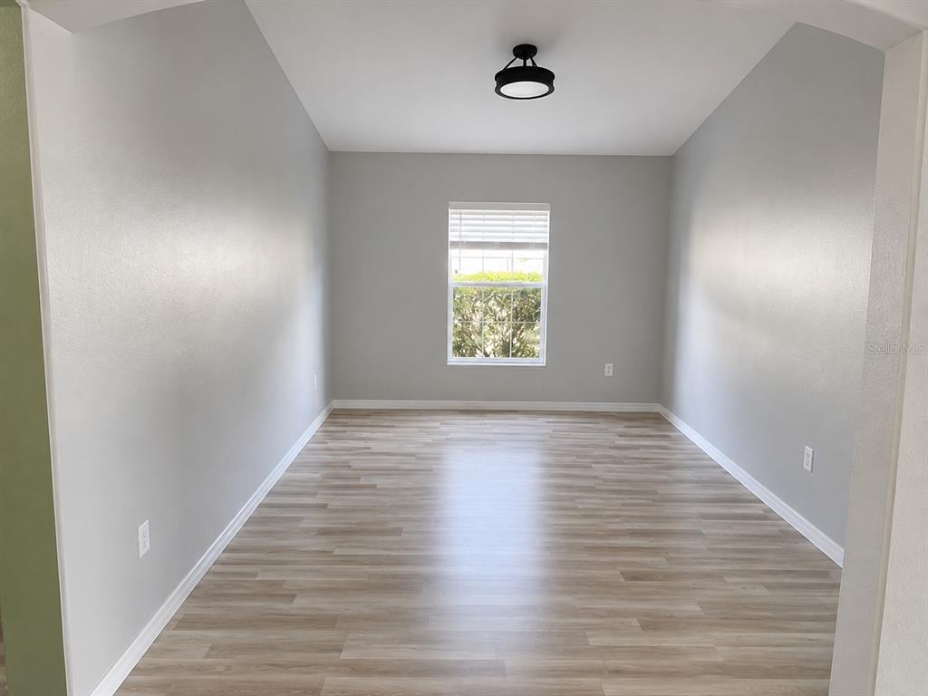 An empty room with light gray walls, wood-look flooring, a single window, and a ceiling light — 2242 COLVILLE CHASE DRIVE, RUSKIN, FL