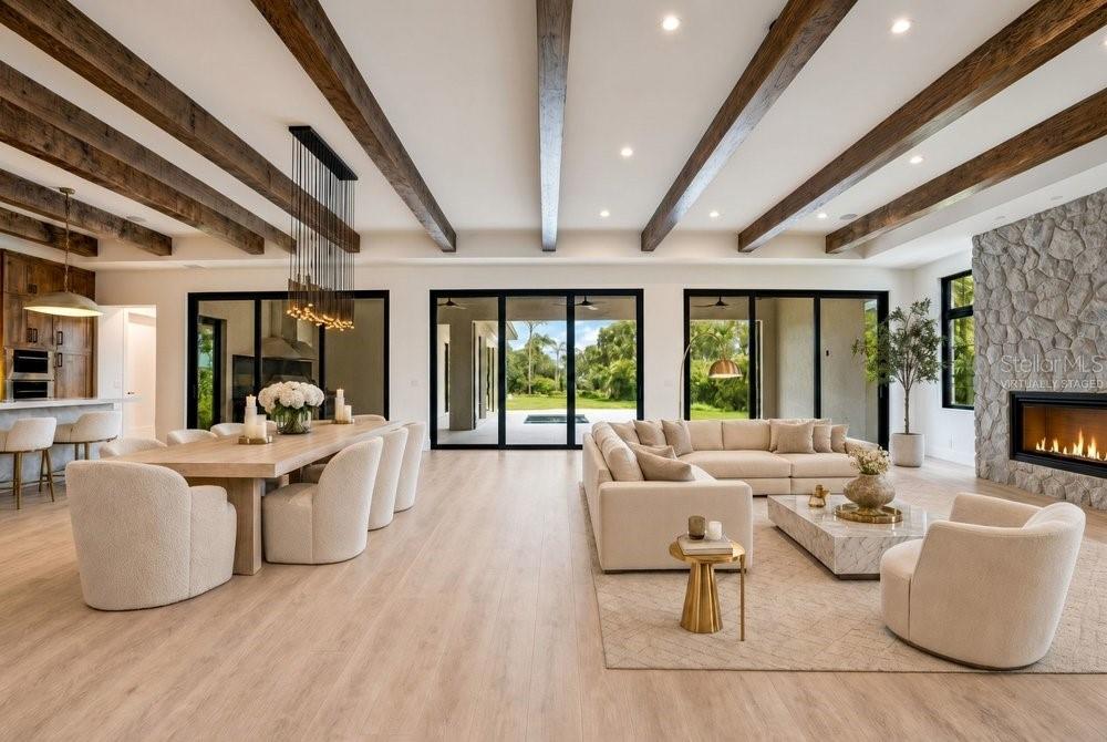 An open-concept living and dining room features wood ceiling beams, a stone fireplace, and glass doors — 8342 BOYLA COURT, WINDERMERE, FL