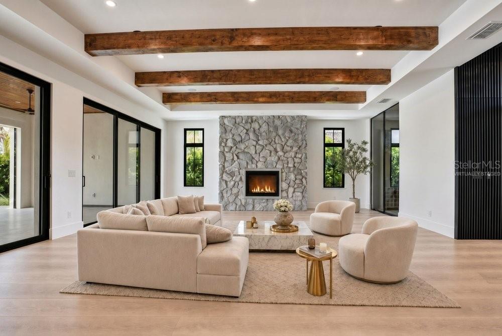 A modern living room features a stone fireplace, exposed wood ceiling beams, and neutral furniture — 8342 BOYLA COURT, WINDERMERE, FL