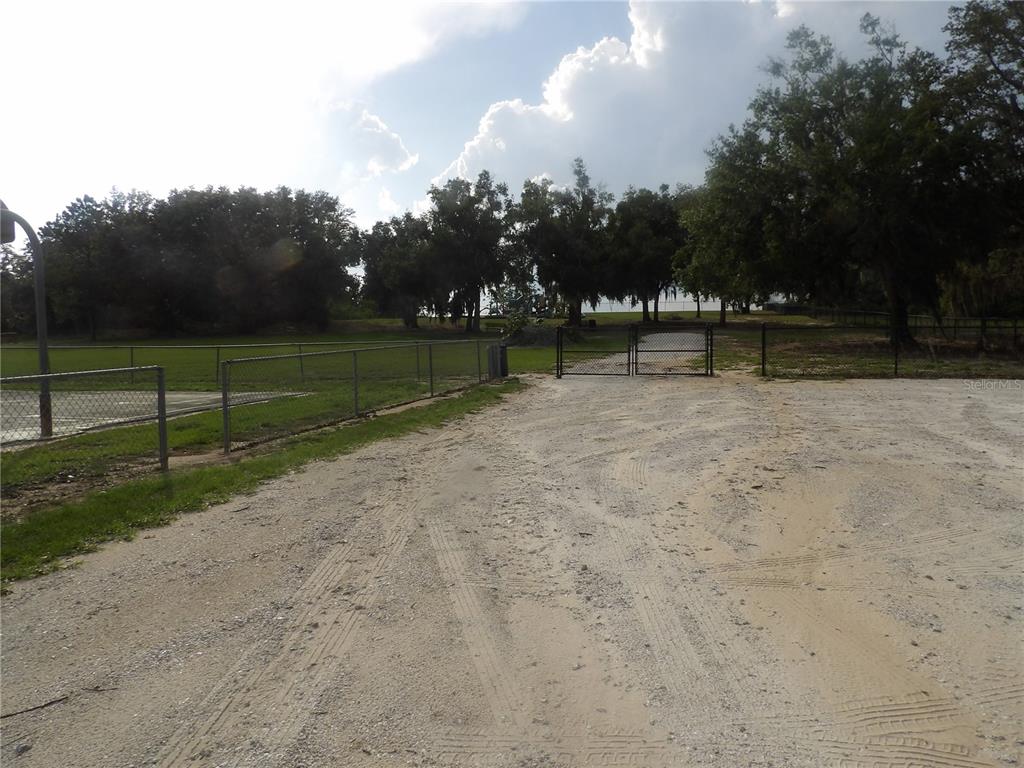 A gravel parking area leads to a fenced park with trees and a sports court — 2817 RICHARDSON ROAD, BARTOW, FL