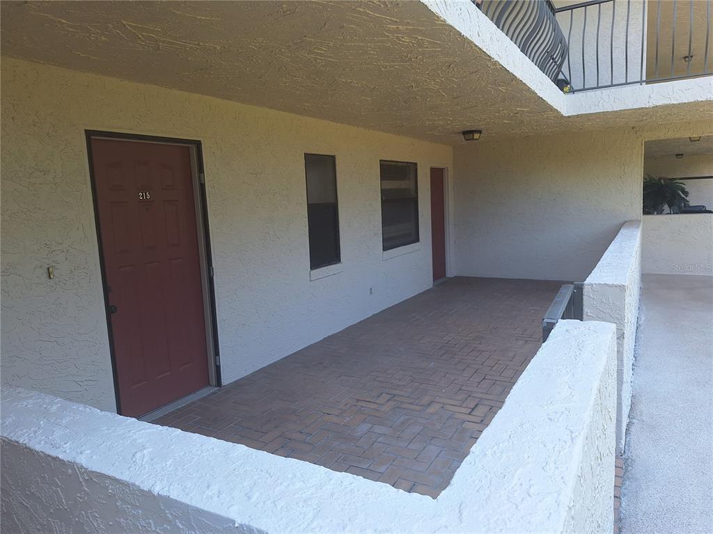 A covered outdoor walkway features a brick-paved floor and a red door marked 215 — 504 S FLORIDA AVENUE UNIT 215, TARPON SPRINGS, FL