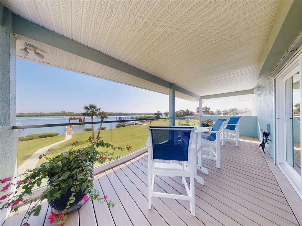 A covered balcony with a glass railing overlooks a grassy lawn and a calm waterway — 2019 S RIVERSIDE, EDGEWATER, FL
