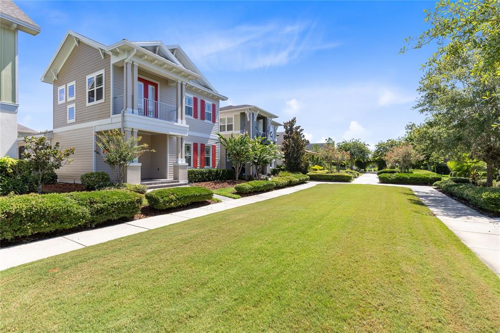 A two-story house with tan siding and red shutters sits beside a grassy lawn — 8460 BERGSON PLACE, ORLANDO, FL