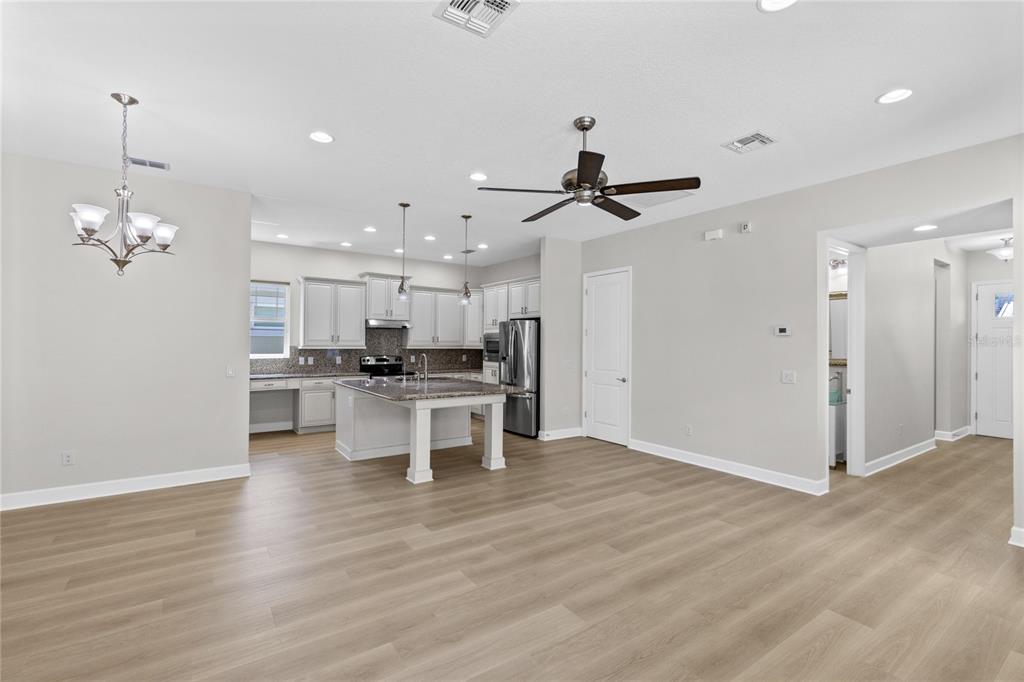 An open-concept kitchen features white cabinetry, a granite-topped island, and light wood-look flooring — 8460 BERGSON PLACE, ORLANDO, FL