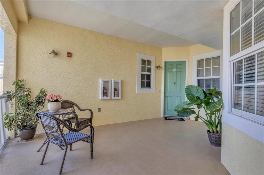 A covered patio features yellow stucco walls, a green front door, and wicker patio furniture — 8561 AMBERJACK CIRCLE UNIT 301, ENGLEWOOD, FL