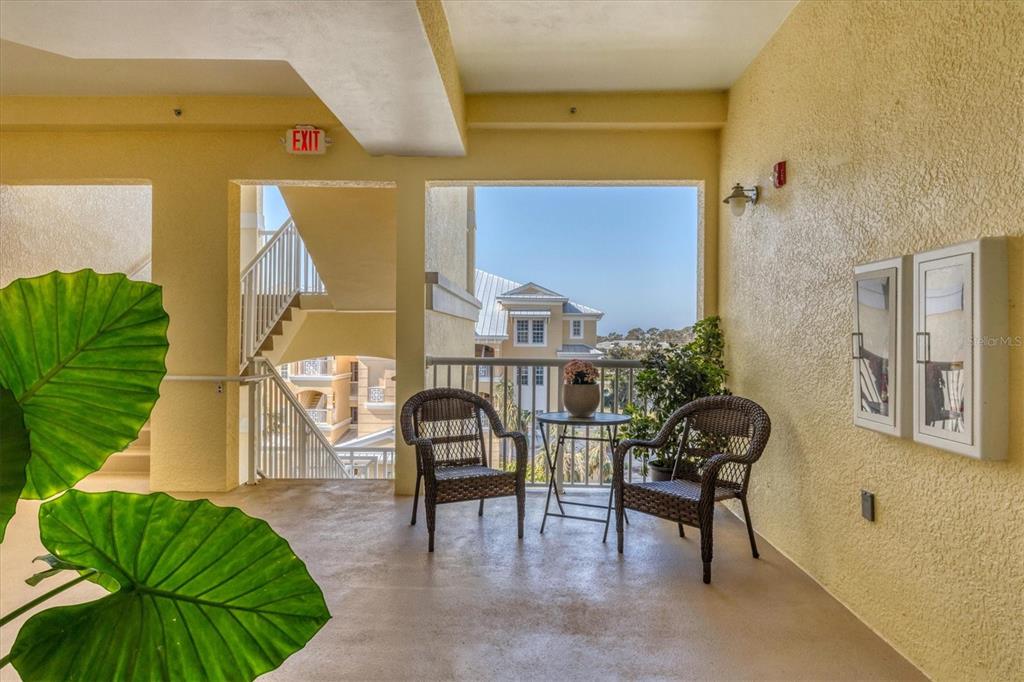 An outdoor balcony features two wicker chairs, a small table, and a view of buildings — 8561 AMBERJACK CIRCLE UNIT 301, ENGLEWOOD, FL