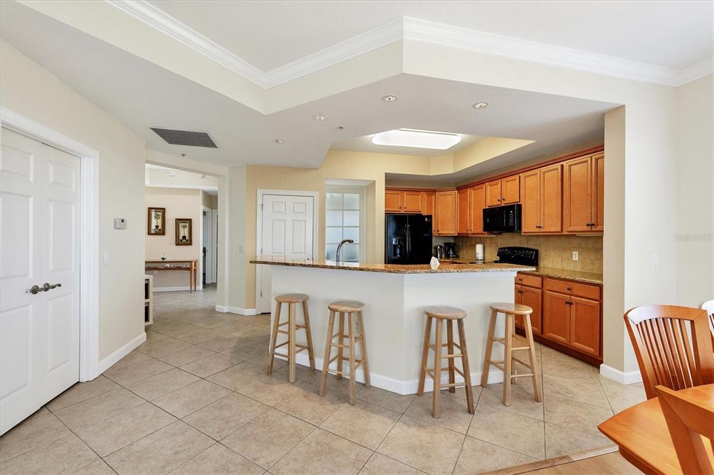 A kitchen with wood cabinets, granite countertops, and a breakfast bar with four wooden stools — 8561 AMBERJACK CIRCLE UNIT 301, ENGLEWOOD, FL