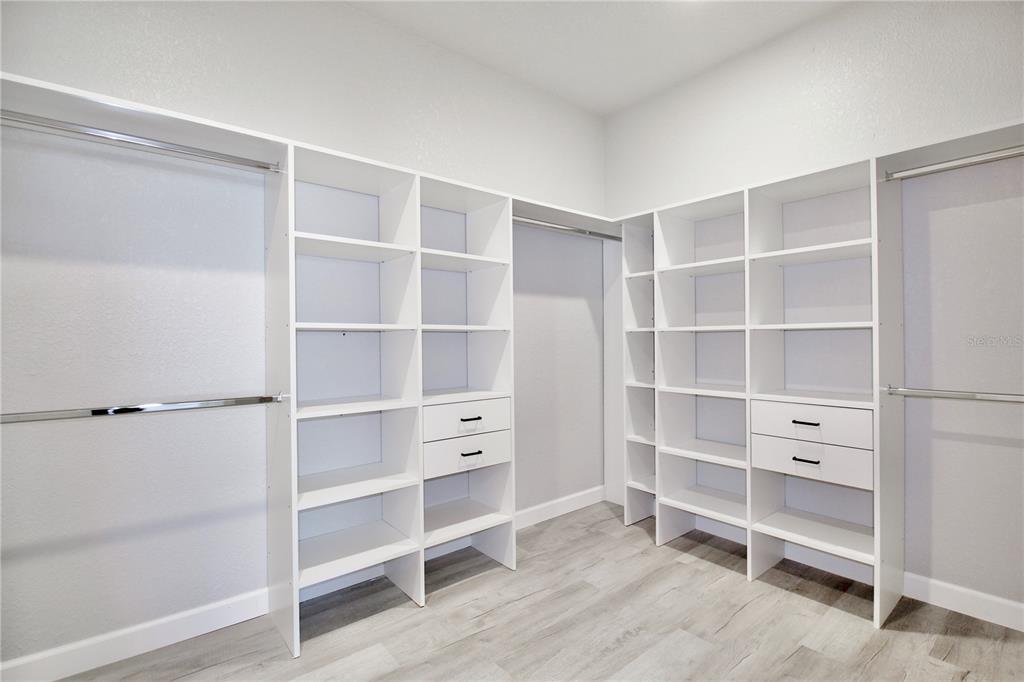 A walk-in closet features white built-in shelving, hanging rods, and light wood-look flooring — 4000 GARIENDA AVENUE, SEBRING, FL
