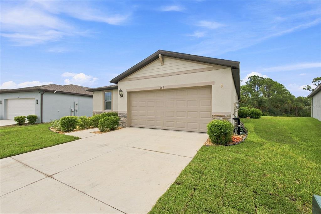 A beige single-story house features a two-car garage, a concrete driveway, and landscaped front lawn — 152 LAZY SHORE DRIVE, NOKOMIS, FL