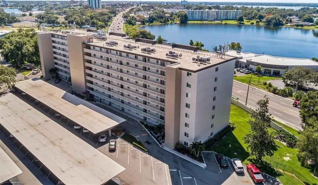 An aerial view shows a multi-story apartment building with a covered parking area and lake — 1776 6TH STREET NW UNIT 504, WINTER HAVEN, FL