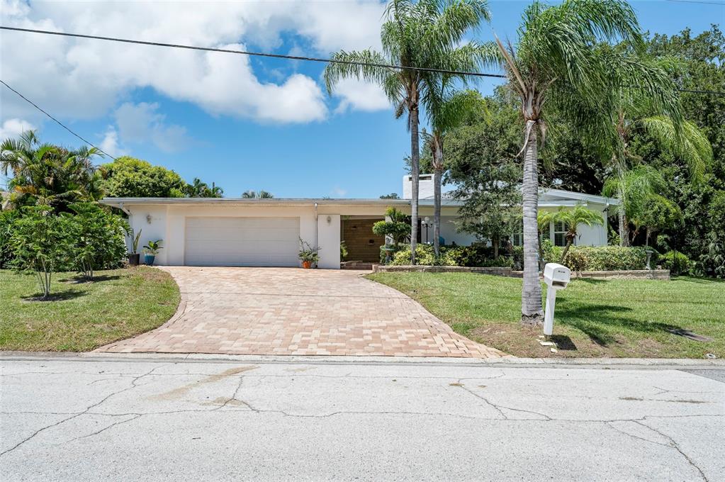 A covered patio features a stone wall, a brown front door, and a wooden deck — 1294 FAIRWAY DRIVE, DUNEDIN, FL