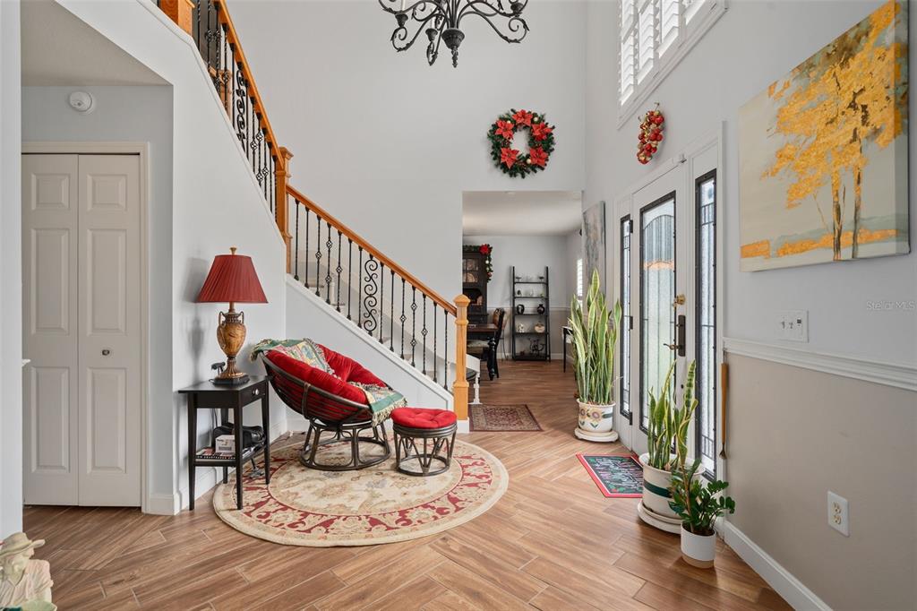 A bright foyer features wood-look tile flooring, a staircase with iron railings, and a seating area — 16017 LANESBORO COURT, CLERMONT, FL