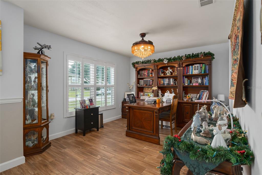A home office features a wooden desk, built-in bookshelves, a display cabinet, and wood-look flooring — 16017 LANESBORO COURT, CLERMONT, FL