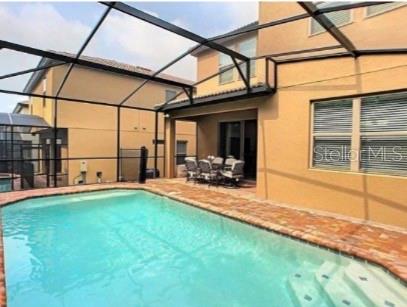 A screened-in swimming pool sits on a brick patio next to a two-story tan house — 1869 NICE COURT, KISSIMMEE, FL