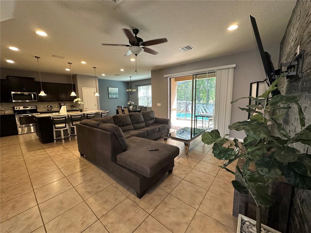 An open-concept living room and kitchen featuring tile floors, a sectional sofa, and pool access — 1869 NICE COURT, KISSIMMEE, FL