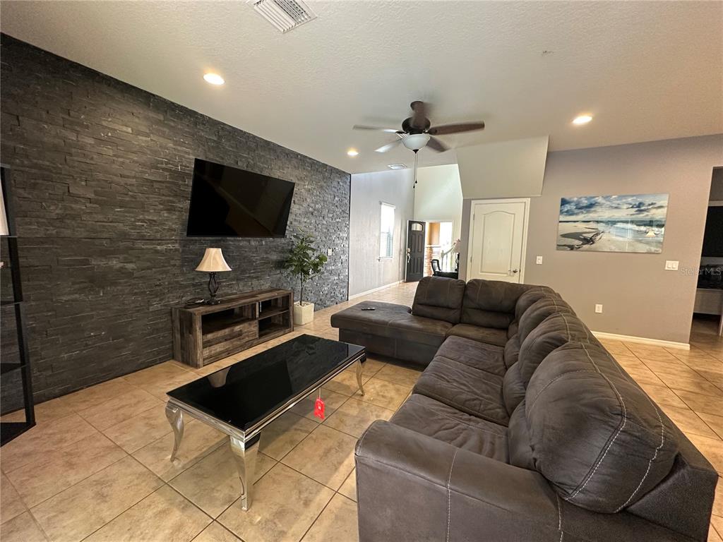 A living room features a dark stone accent wall, a sectional sofa, and tile flooring — 1869 NICE COURT, KISSIMMEE, FL