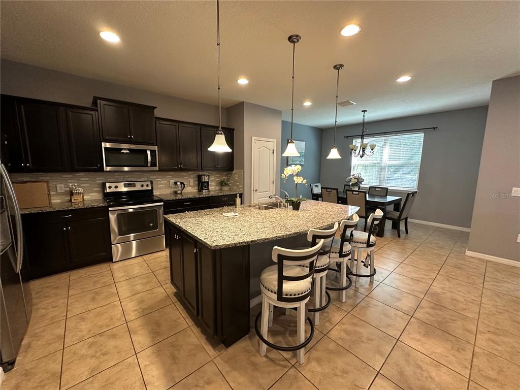 A kitchen features dark wood cabinets, granite countertops, a large island, and tile flooring — 1869 NICE COURT, KISSIMMEE, FL