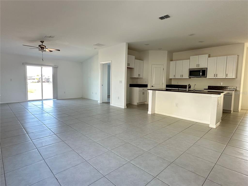 An open-concept kitchen with white cabinets and a breakfast bar overlooks a large tiled living area — 5380 BLUE HORIZON WAY, WIMAUMA, FL