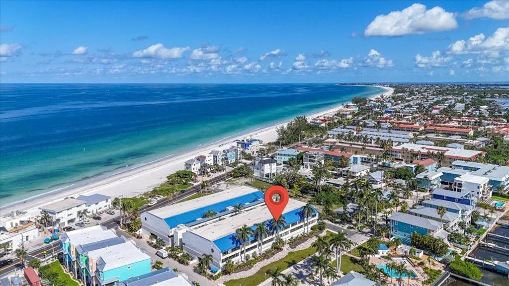 An aerial view shows a multi-story building with a blue roof near a sandy beach — 1007 GULF DRIVE N UNIT 217, BRADENTON BEACH, FL