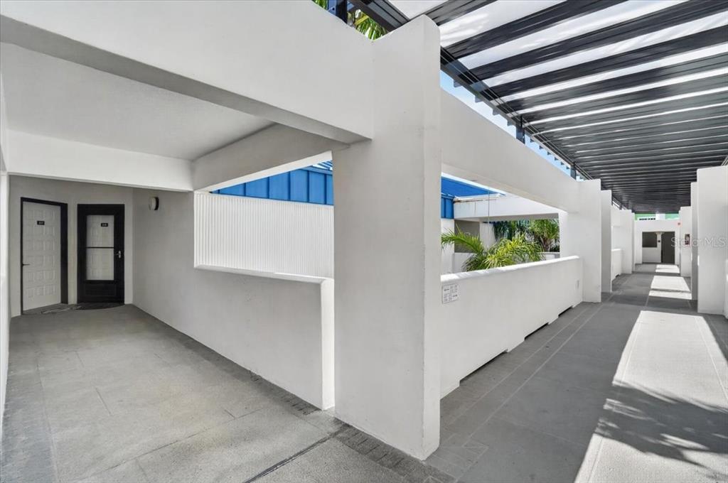 An outdoor walkway features white concrete walls, a slatted metal roof, and two dark doors — 1007 GULF DRIVE N UNIT 217, BRADENTON BEACH, FL