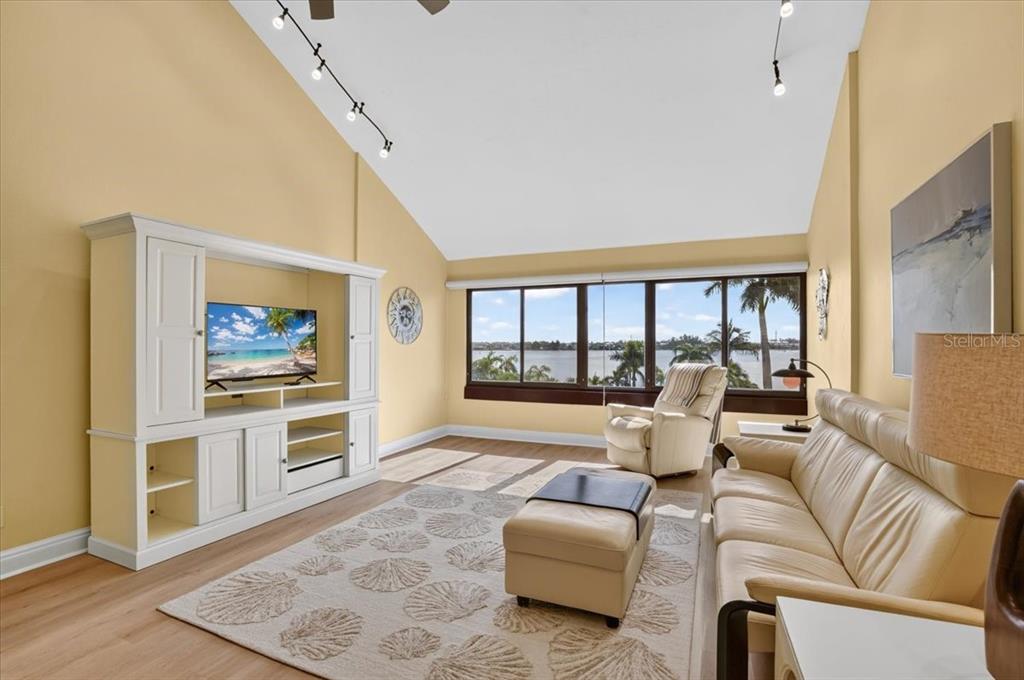 A living room with vaulted ceilings, a white entertainment center, and a view of water — 1007 GULF DRIVE N UNIT 217, BRADENTON BEACH, FL