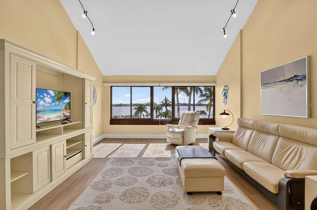 A living room with a vaulted ceiling, beige walls, leather sofa, and a waterfront view — 1007 GULF DRIVE N UNIT 217, BRADENTON BEACH, FL