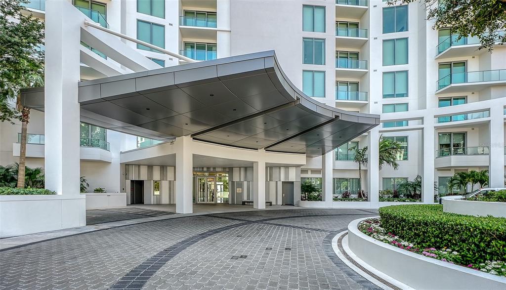 An exterior view of a modern building entrance featuring a curved metal porte-cochère — 401 QUAY COMMONS UNIT 505, SARASOTA, FL