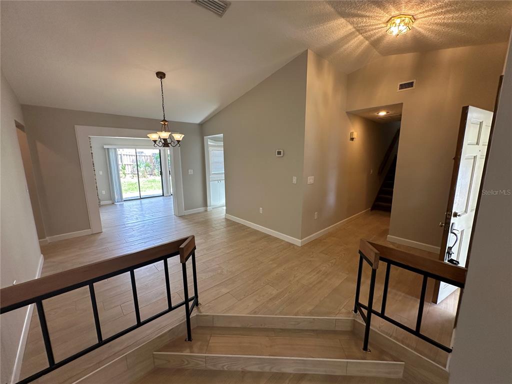 An entryway with light wood-look tile flooring leads to a sunken living area with stairs — 840 MARAVAL COURT, LONGWOOD, FL
