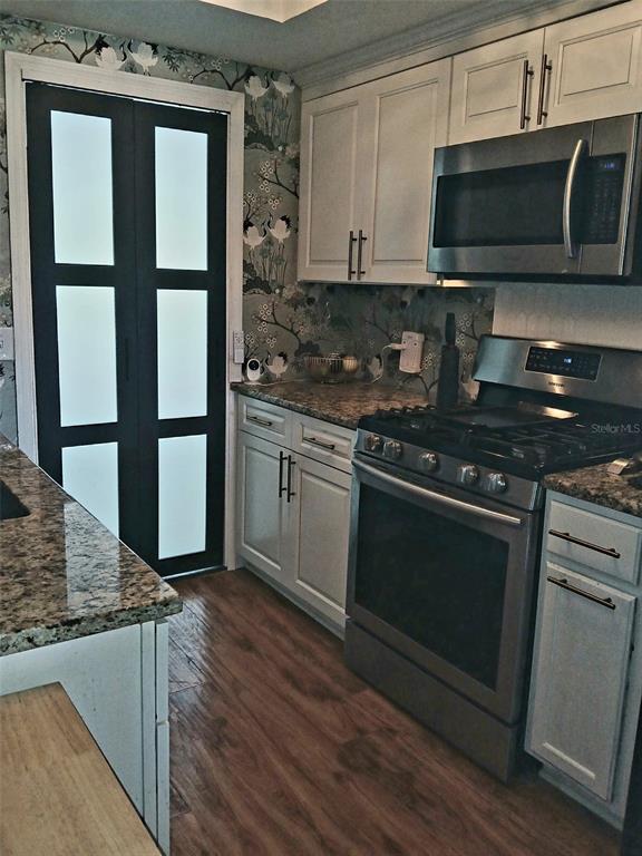 A kitchen features white cabinetry, granite countertops, stainless steel appliances, and patterned floral wallpaper — 1900 59TH AVENUE N UNIT 312, ST PETERSBURG, FL