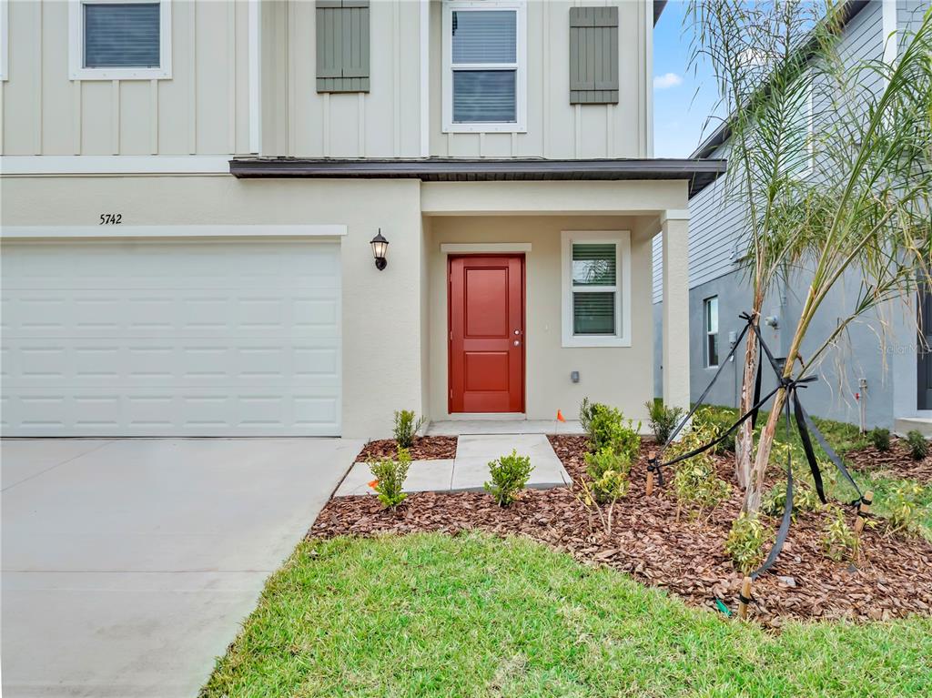 A two-story house exterior features a white garage, a red front door, and landscaping — 2215 RED CROSSBILL DRIVE, WIMAUMA, FL