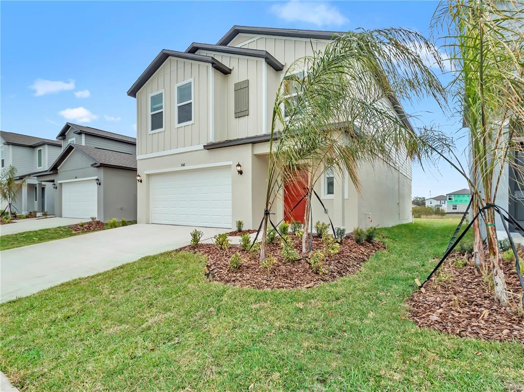 A two-story suburban house with beige siding, a two-car garage, and a red front door — 2215 RED CROSSBILL DRIVE, WIMAUMA, FL