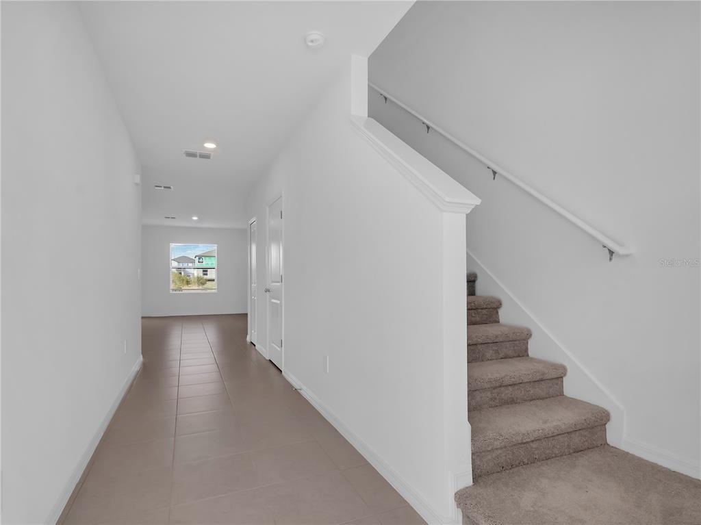 A hallway with tiled flooring leads to a window, with carpeted stairs on the right — 2215 RED CROSSBILL DRIVE, WIMAUMA, FL