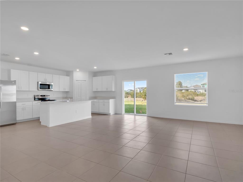 A kitchen with white cabinets and a tile floor opens into a spacious living area — 2215 RED CROSSBILL DRIVE, WIMAUMA, FL