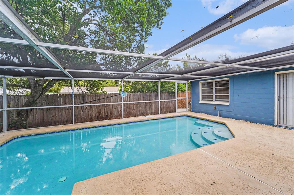 A screened-in swimming pool with a concrete deck sits beside a blue house exterior — 9540 RAINBOW LANE, PORT RICHEY, FL