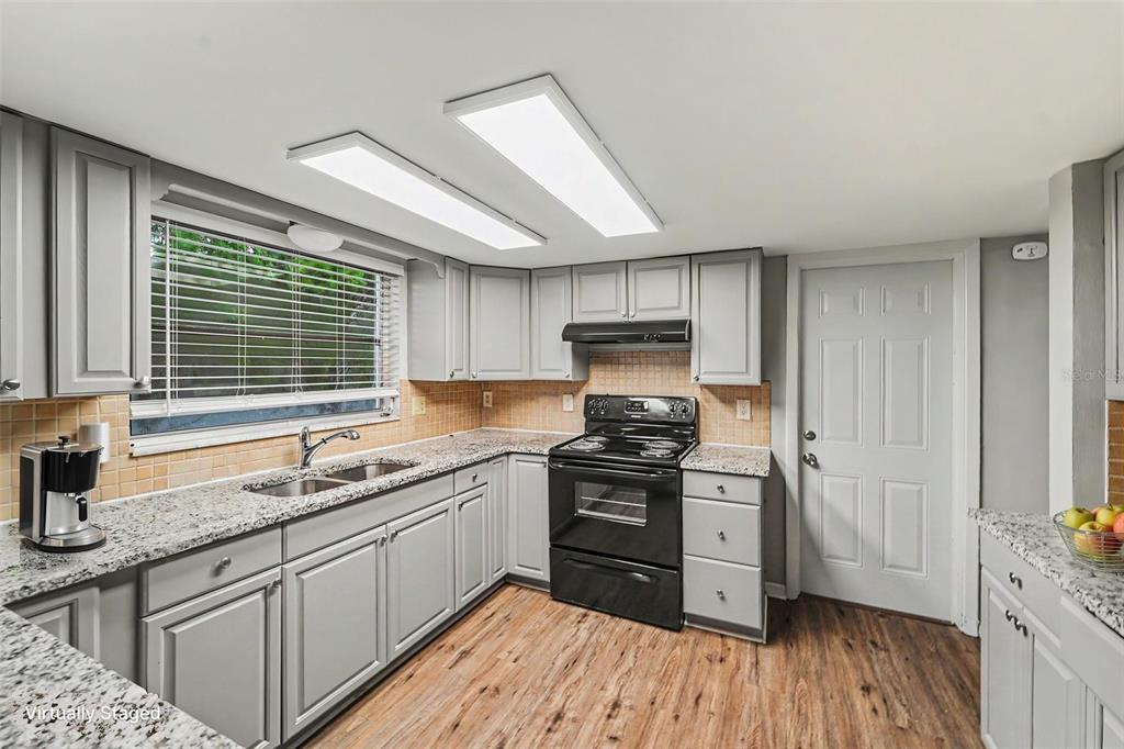 A kitchen with gray cabinets, granite countertops, a black stove, and wood-look flooring — 9540 RAINBOW LANE, PORT RICHEY, FL