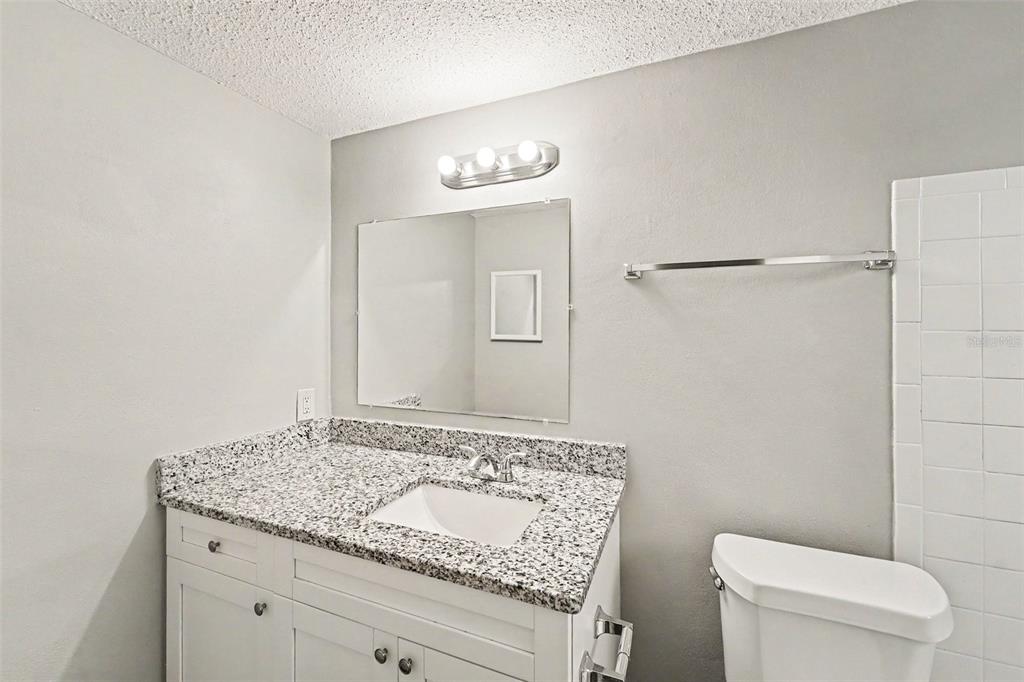 A bathroom features a white vanity with a granite countertop, a mirror, and a toilet — 9540 RAINBOW LANE, PORT RICHEY, FL