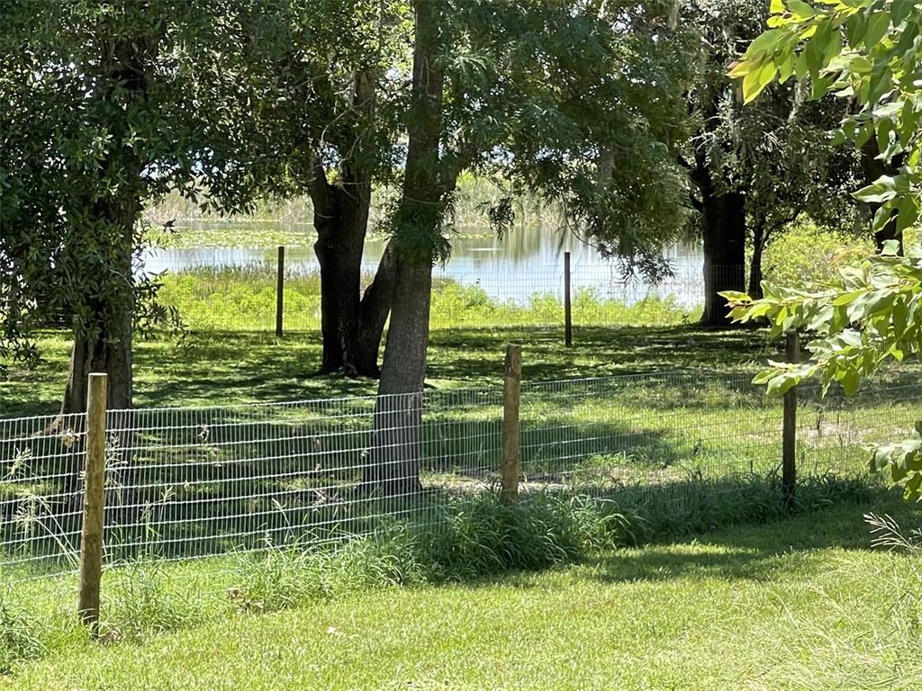A wire fence encloses a grassy yard with mature trees overlooking a pond — A T RACE ROAD, DUNDEE, FL