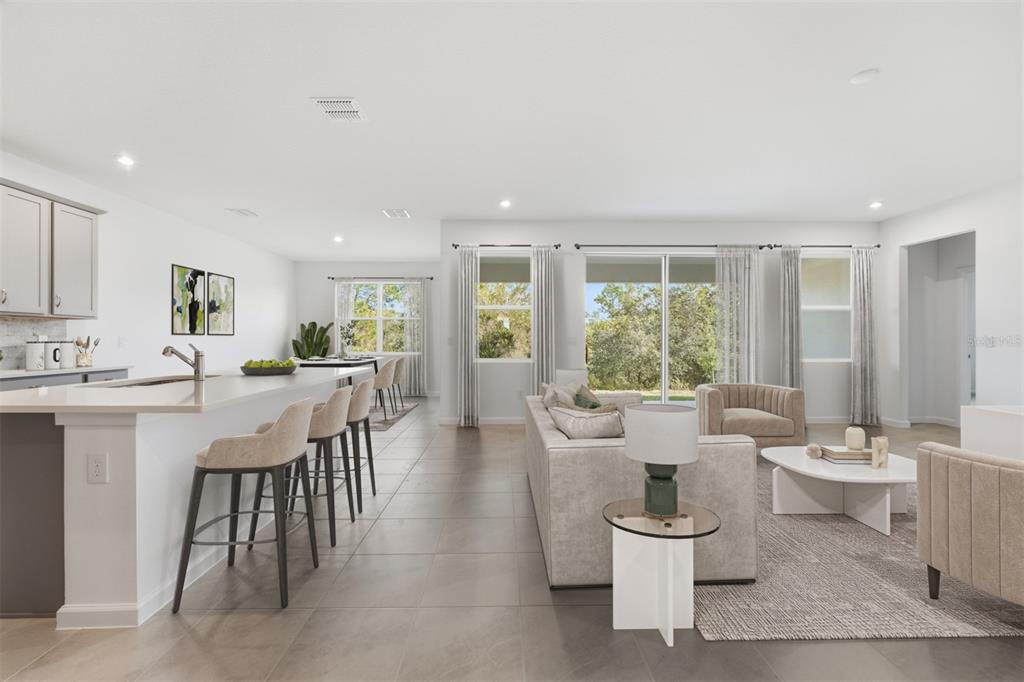 An open-concept kitchen and living area with a breakfast bar, neutral furniture, and tile flooring — 324 FREE RANGE DRIVE, GROVELAND, FL